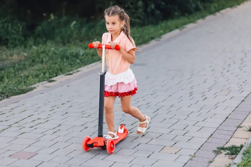 cute girl riding red-push scooter walkway